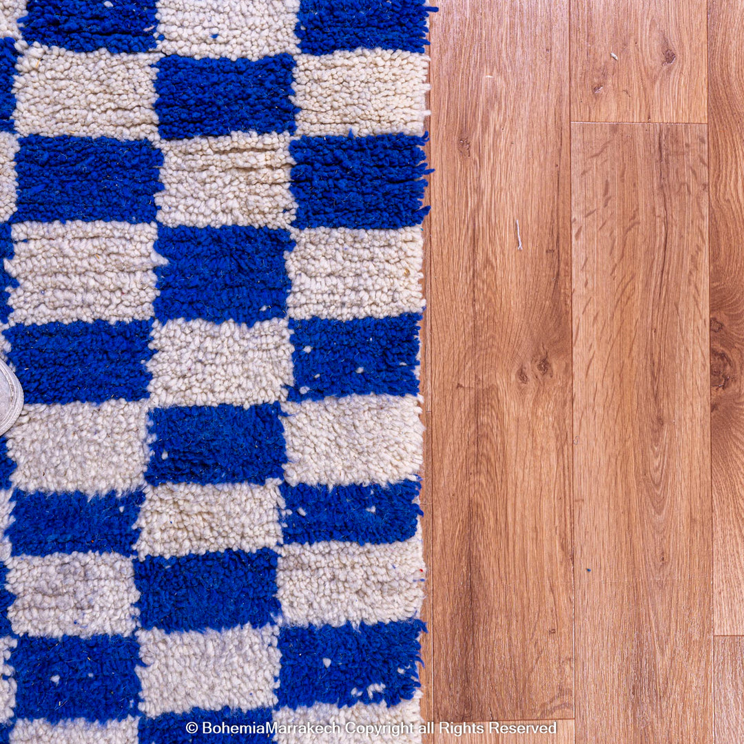 Blue and white checkered Moroccan wool rug on hardwood floor, showcasing traditional Berber weaving and modern design style.