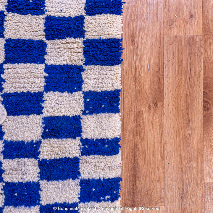Blue and white checkered Moroccan wool rug on hardwood floor, showcasing traditional Berber weaving and modern design style.