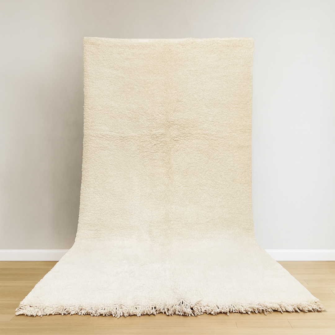 Beige rug with fringes on a wooden floor against a white wall