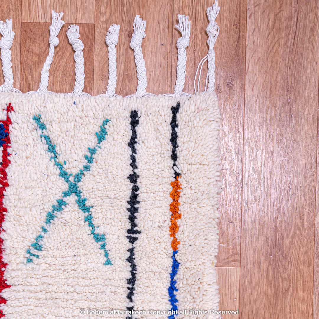 Corner of colorful Azilal Moroccan wool rug with geometric patterns on a wooden floor.