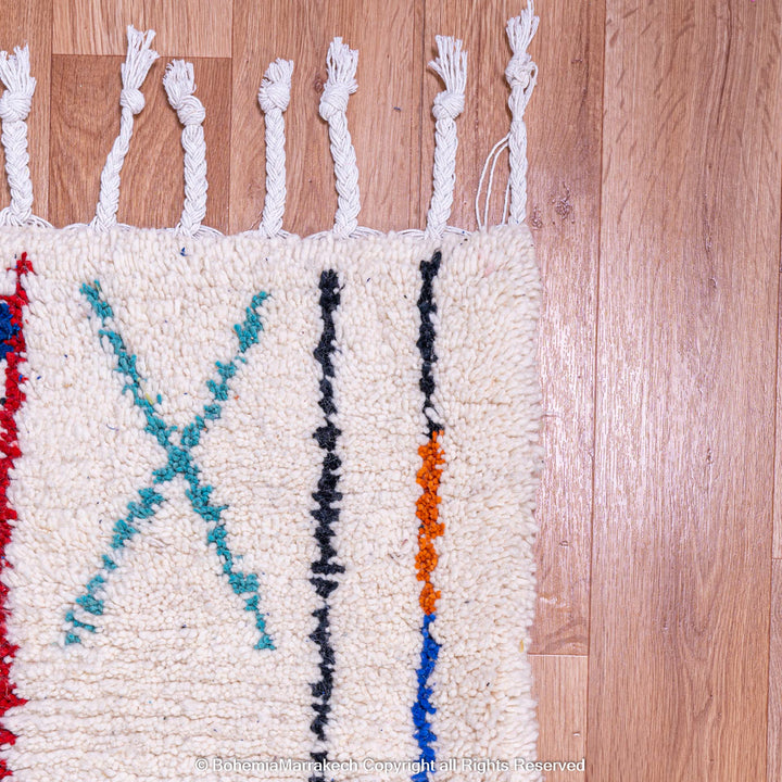 Corner of colorful Azilal Moroccan wool rug with geometric patterns on a wooden floor.