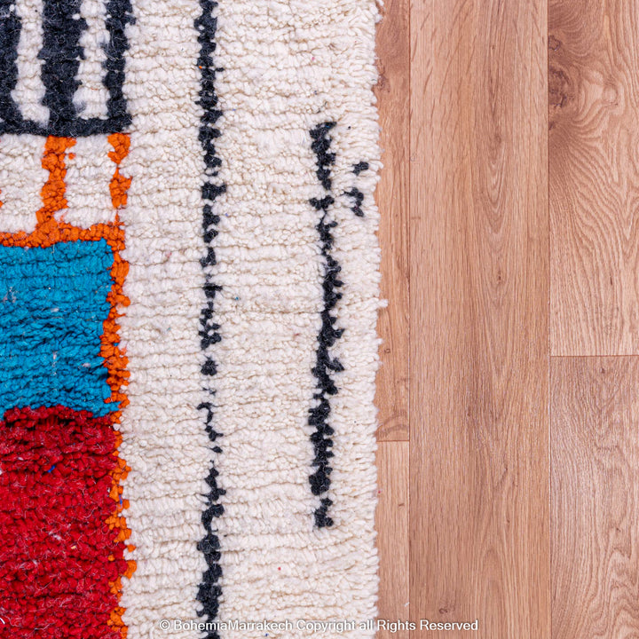 Colorful geometric Moroccan rug with cream background and bold motifs on wood floor.