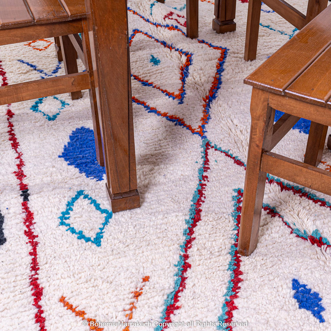 Colorful Azilal Moroccan rug with geometric patterns in blue, red, orange, and teal under wooden furniture.