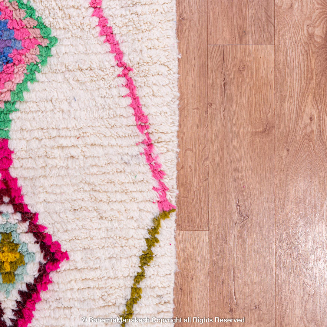 Colorful Moroccan rug with Azilal diamond motifs against a wooden floor.
