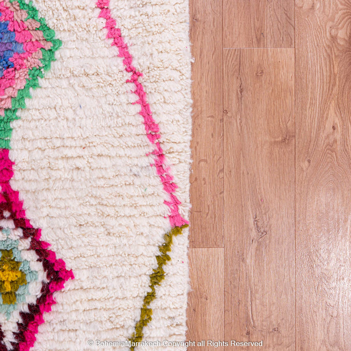 Colorful Moroccan rug with Azilal diamond motifs against a wooden floor.