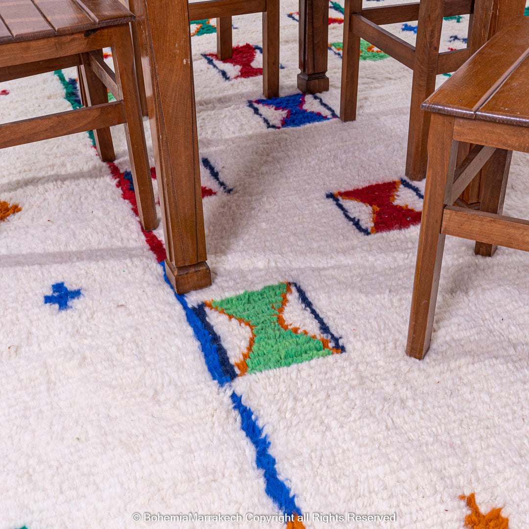 Colorful Moroccan rug with Berber X and cross symbols under a wooden dining set, featuring vibrant geometric patterns on an ivory base.