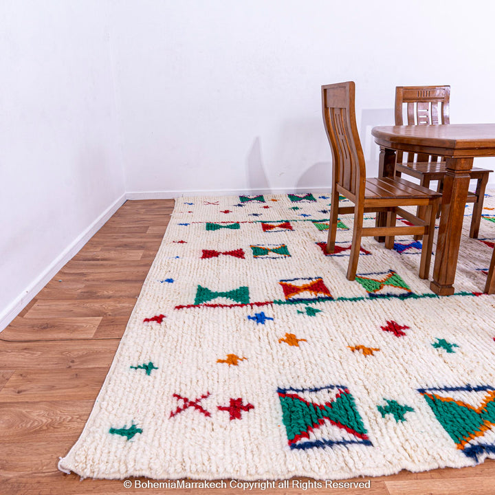 Colorful Moroccan rug with Berber X and cross symbols on ivory base under a wooden dining set.