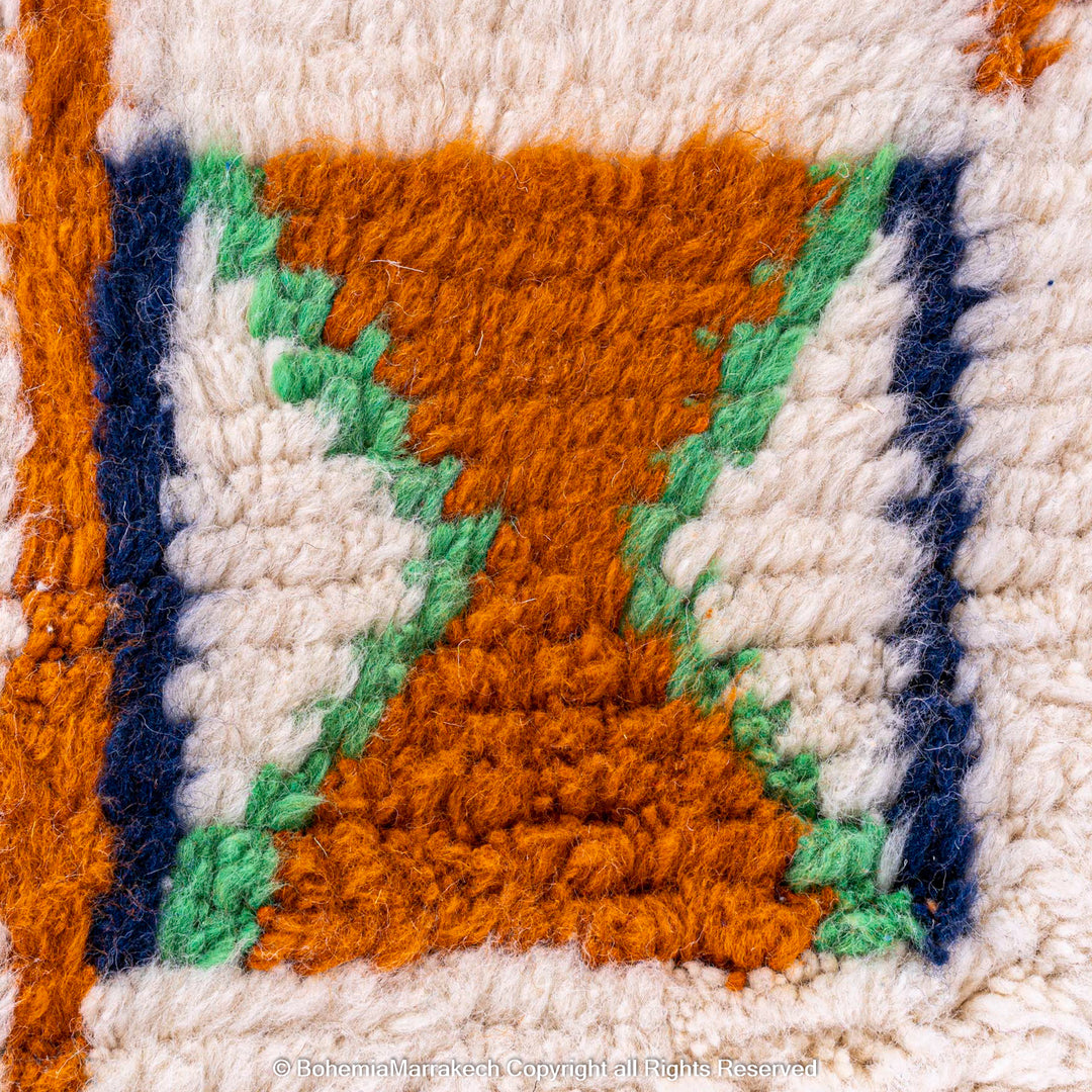 Close-up of traditional Moroccan Berber rug with X and cross symbols, featuring orange, green, and blue on an ivory wool base.