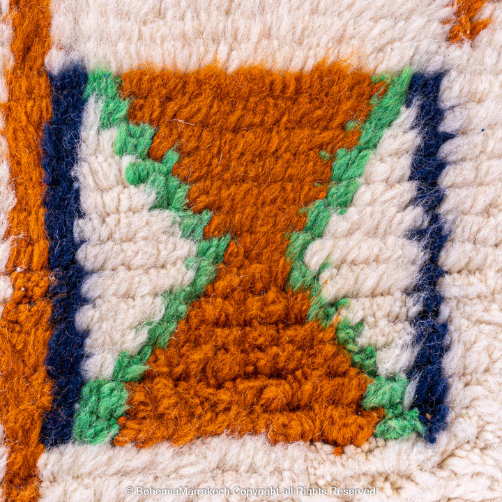 Close-up of traditional Moroccan Berber rug with X and cross symbols, featuring orange, green, and blue on an ivory wool base.