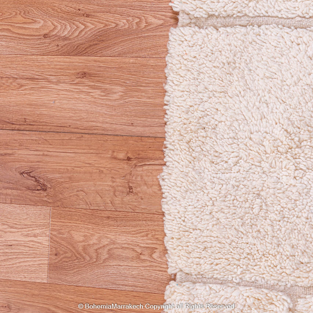 Minimalist Moroccan rug with off-white wool, showcasing Berber craftsmanship and geometric patterns on wooden floor.