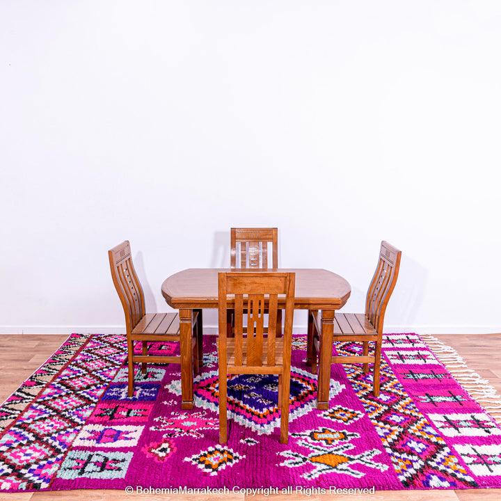 Colorful Boujad Moroccan rug with magenta and purple tribal motifs under wooden dining set.