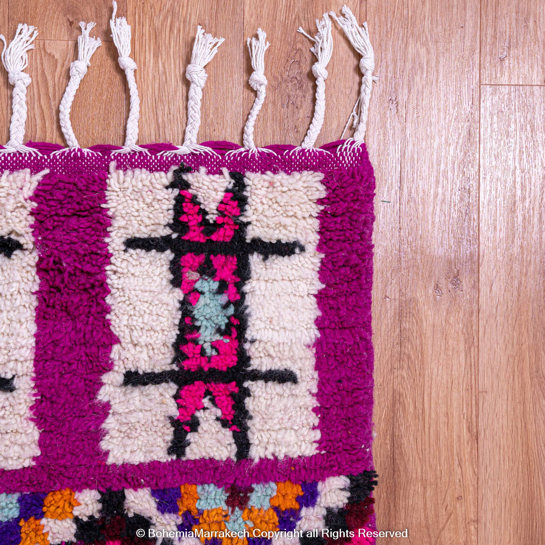 Colorful Boujad Moroccan rug with pink and purple wool, tribal motifs, on wooden floor.