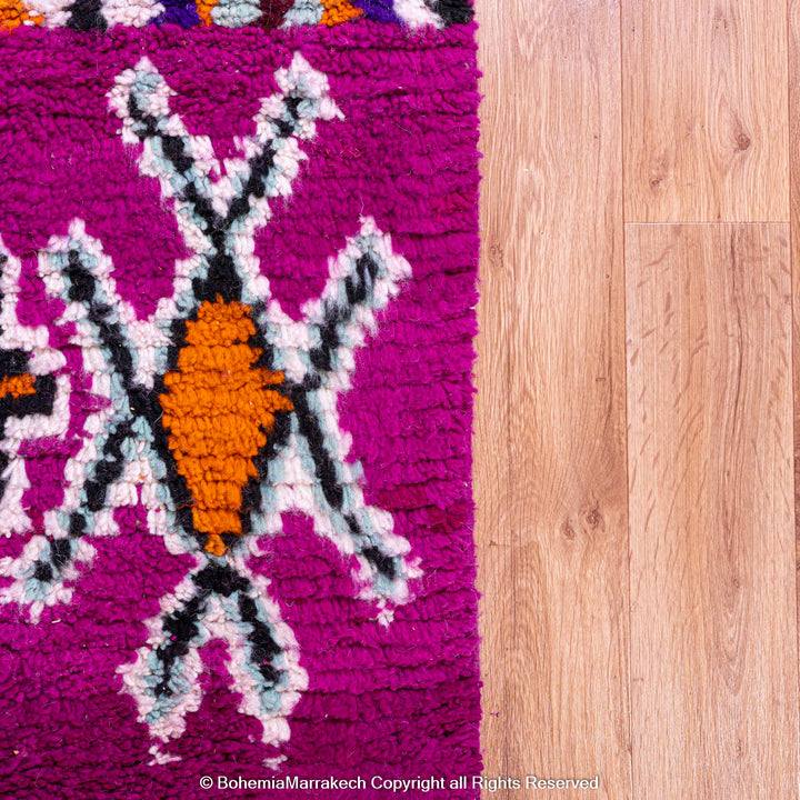 Colorful Boujad Moroccan rug with magenta and purple tribal designs, handmade from wool by Berber artisans, styled on wood flooring.