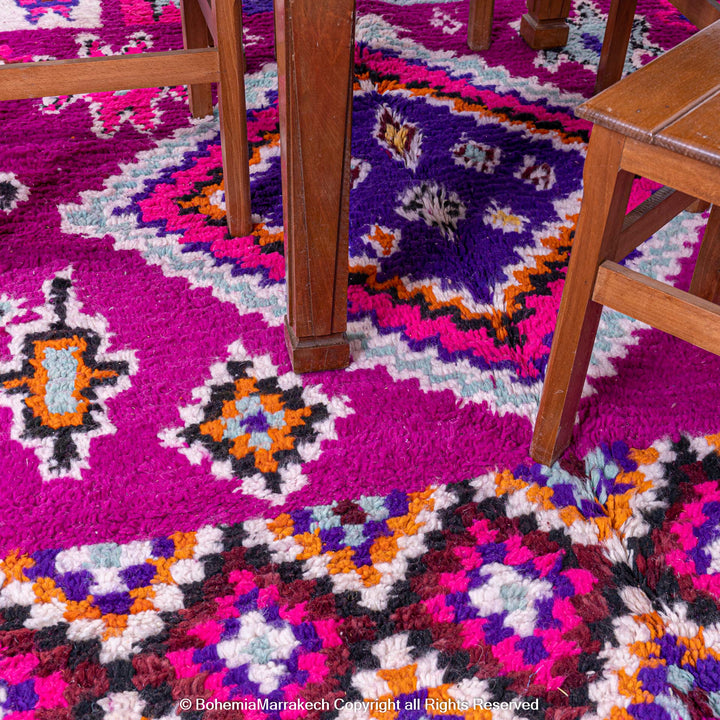 Colorful Boujad Moroccan wool rug with pink and purple tribal designs under wooden chairs, handmade by Berber artisans.