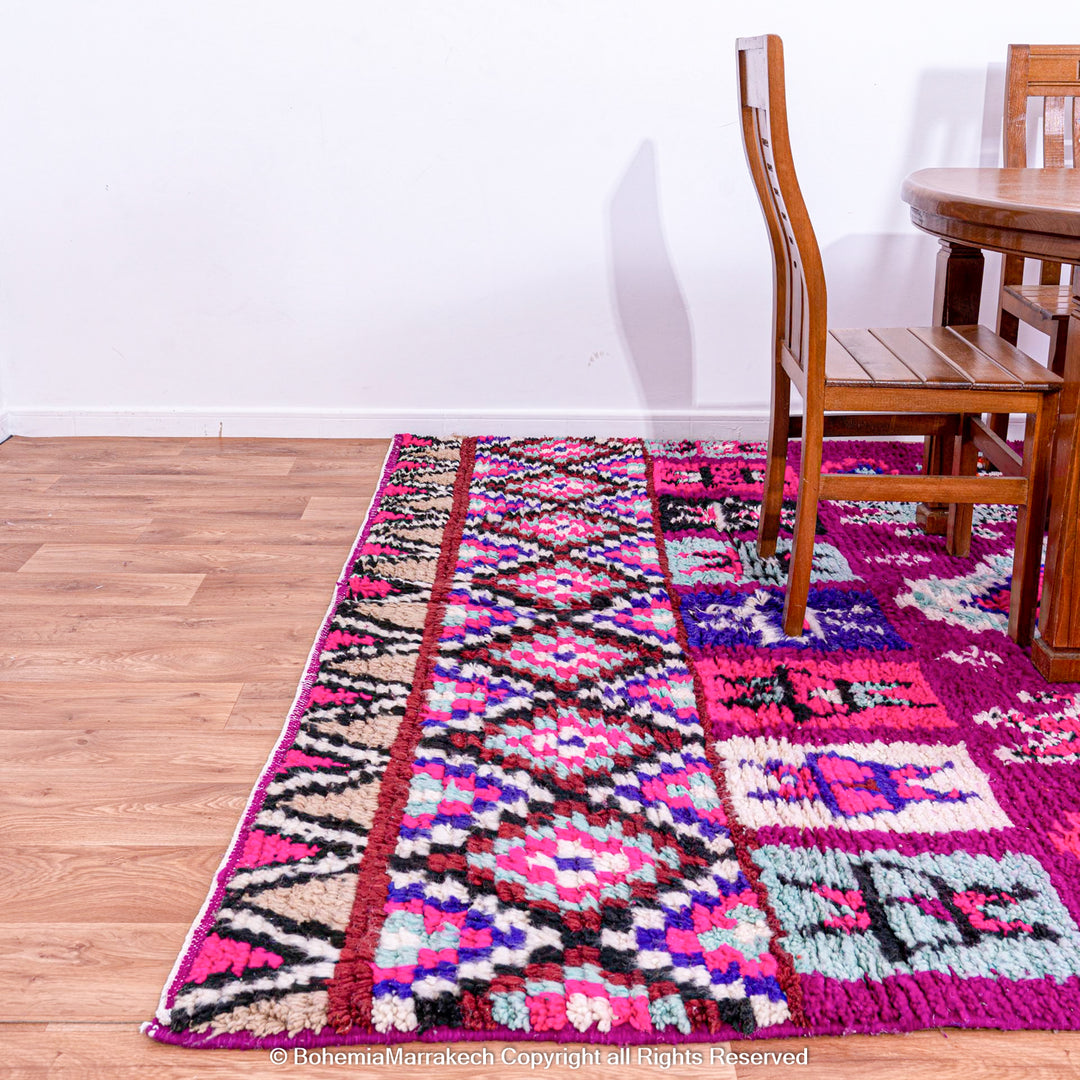 Colorful Boujad Moroccan rug with pink and purple tribal designs, handcrafted by Berber artisans from wool, displayed in a dining area.
