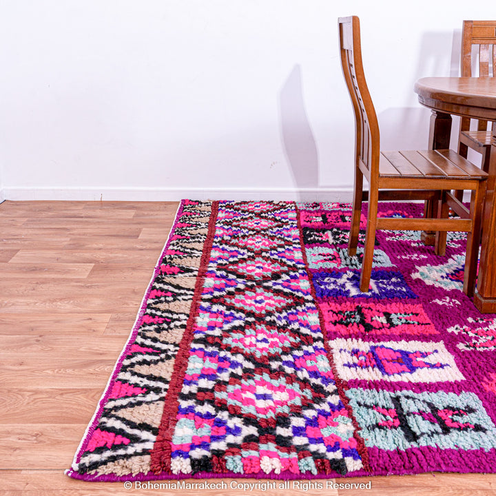 Colorful Boujad Moroccan rug with pink and purple tribal designs, handcrafted by Berber artisans from wool, displayed in a dining area.