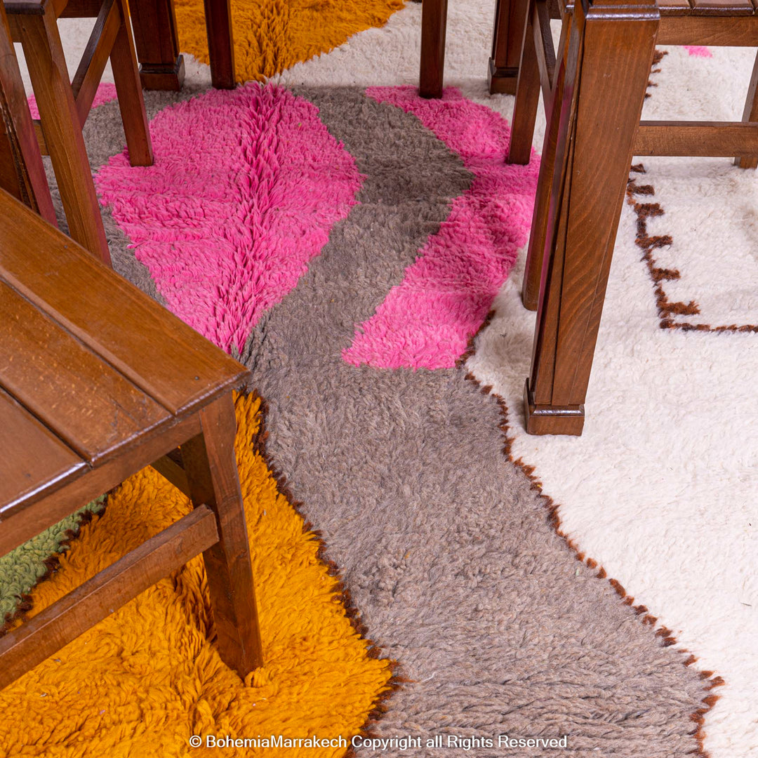 Handmade colorful Moroccan rug with pink, yellow, brown, and green geometric patterns on white wool