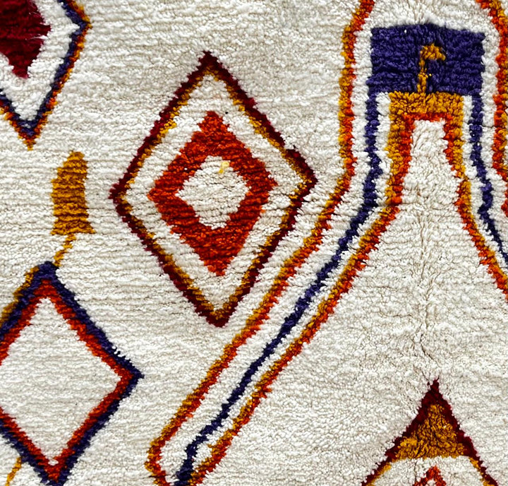 Handmade Moroccan wool runner rug with geometric Berber motifs in terracotta, mustard, blue, and purple on a cream background