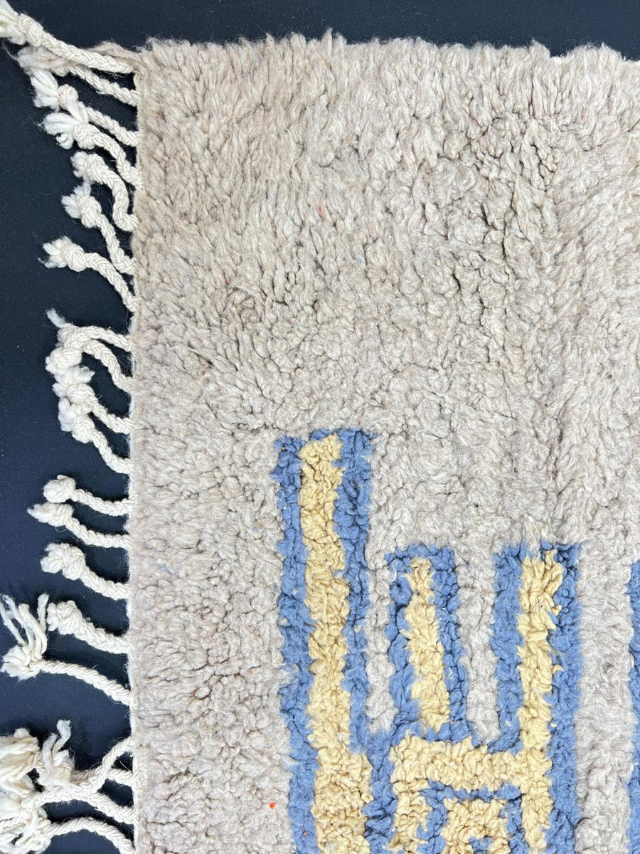 Golden Moroccan wool runner rug with blue geometric border and neutral background, handmade by Berber artisans