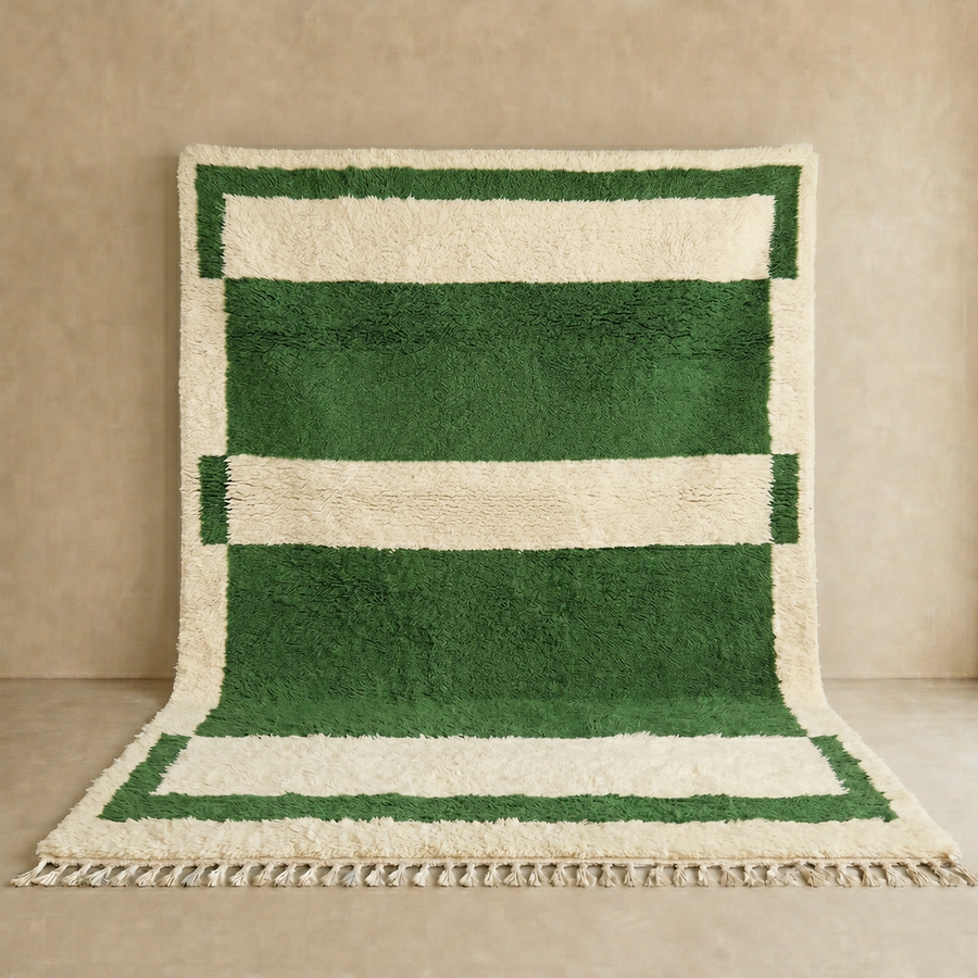 Green and cream handmade Moroccan wool rug with bold geometric border design, plush texture, and fringed tassels, displayed against a neutral beige wall.