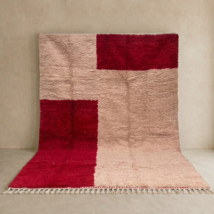 Handwoven Moroccan wool rug with blush pink and deep red geometric blocks, soft shag texture, and white tassel fringe.
