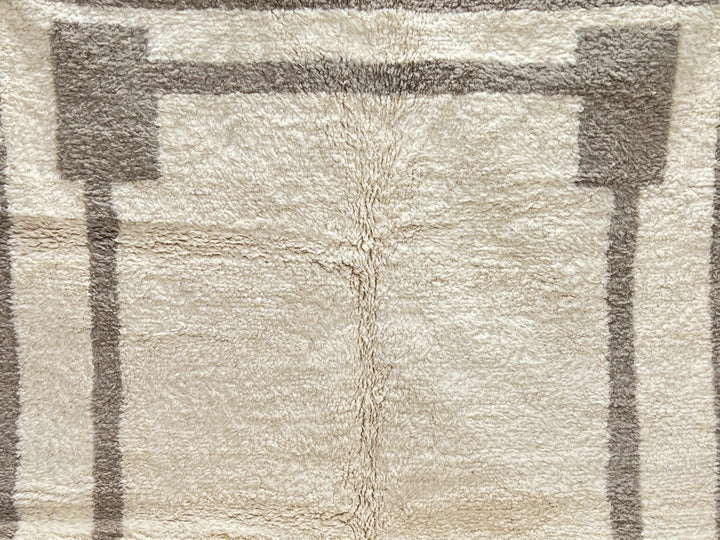 Textured area rug with geometric pattern on a dark floor against a light brick wall.