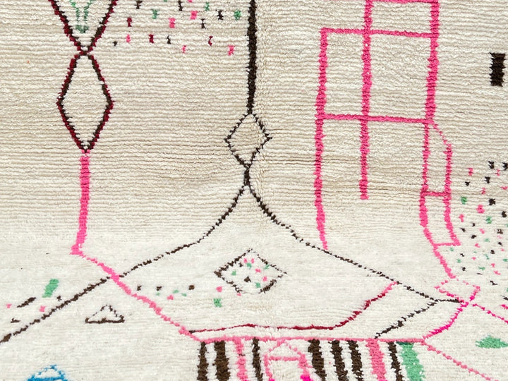 Decorative rug with geometric pattern on a dark floor against a light brick wall.