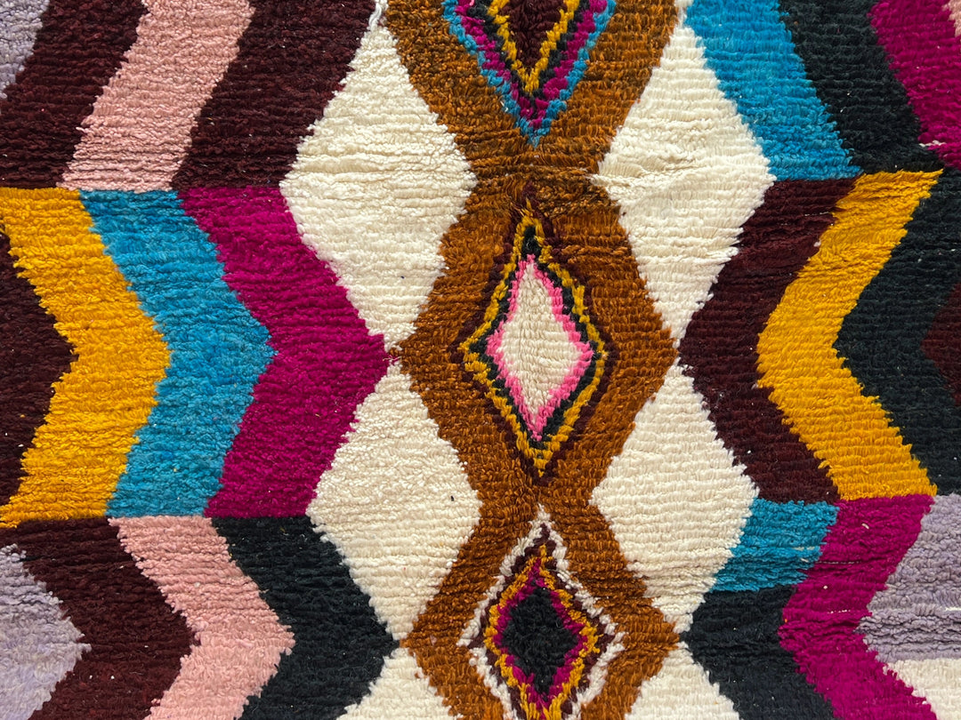 Multicolored geometric patterned rug against a white brick wall.