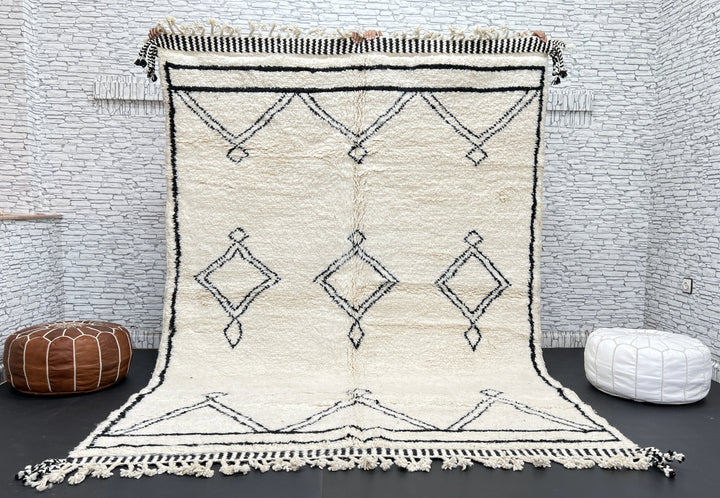 Beige and black patterned rug with tassels on a dark floor against a white brick wall.