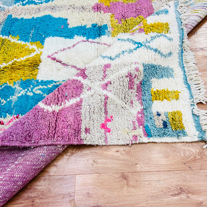 Vintage Moroccan Berber rug 8.5x5.3 ft with pink, blue, mustard abstract design, handwoven wool, on wood floor