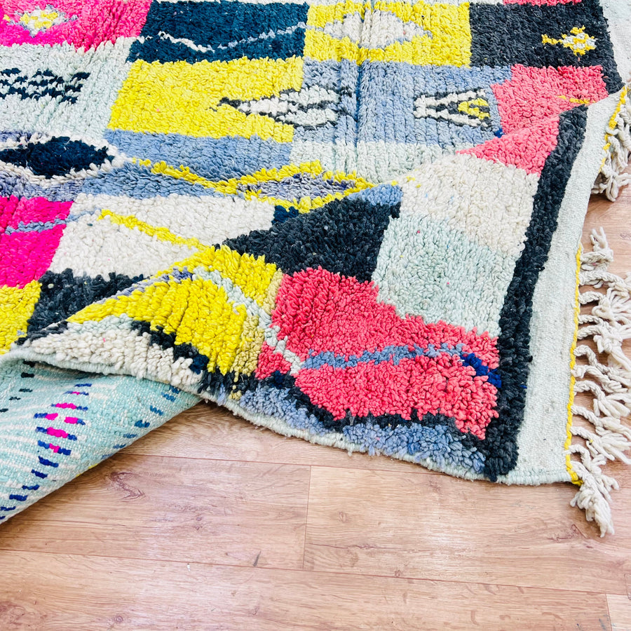 Colorful vintage Moroccan wool rug with bold tribal symbols in pink, yellow, blue, and black, showcasing Berber artistry.