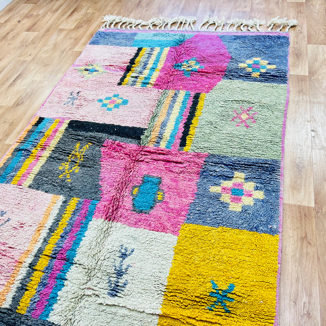 Colorful vintage Moroccan Berber rug with patchwork design, featuring pink, yellow, blue, and charcoal geometric patterns.