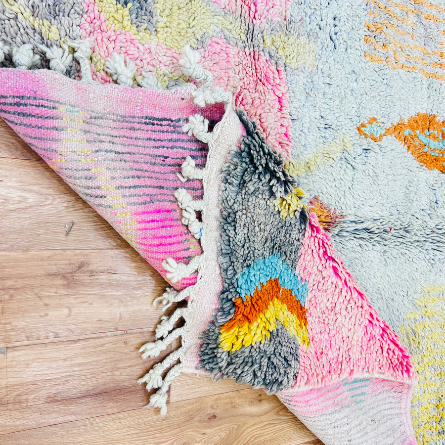 Vintage Moroccan wool rug with colorful tribal patterns and tassels, handmade by Berber artisans, displayed on a wooden floor.