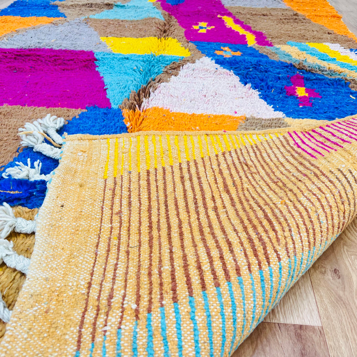 Vintage Moroccan rug with geometric patchwork in earth tones, pink, turquoise, and blue, crafted from natural wool by Berber artisans.