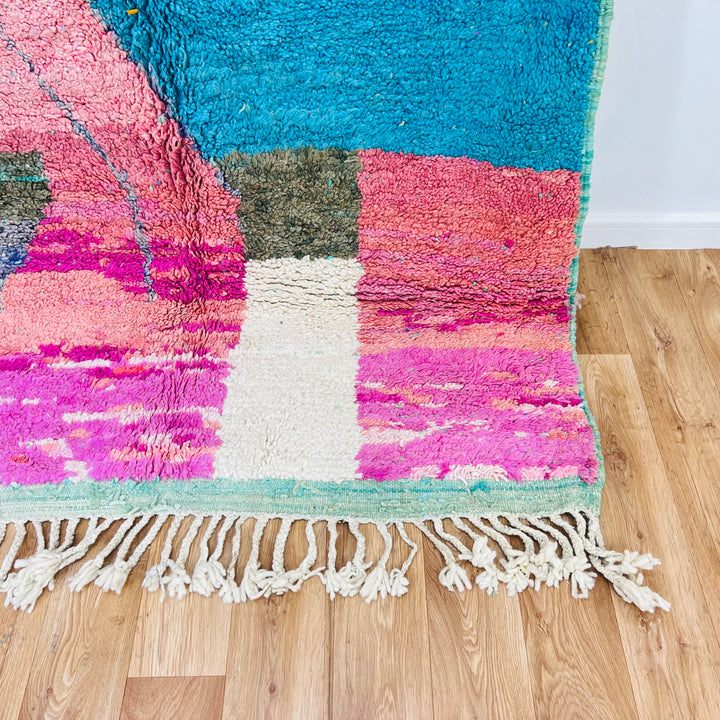 Colorful Moroccan Berber rug with fuchsia, turquoise, and orange blocks on wood floor. Handmade wool area rug from Morocco.