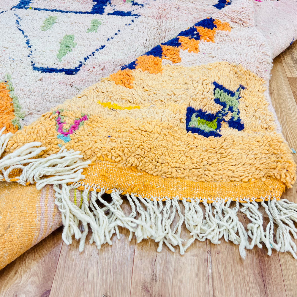 Close-up of colorful tribal diamond Moroccan rug with Berber symbols and white fringe, handwoven with wool on a wooden floor.
