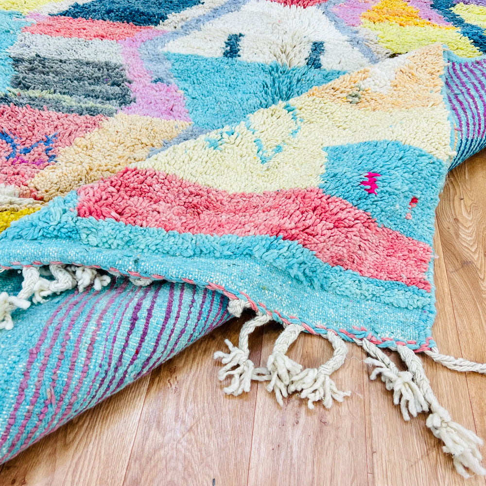 Colorful geometric Moroccan wool rug with vibrant turquoise, pink, yellow, and lavender design, handwoven by Berber artisans.