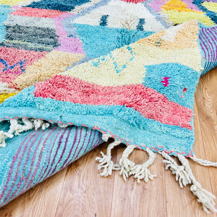 Colorful geometric Moroccan wool rug with vibrant turquoise, pink, yellow, and lavender design, handwoven by Berber artisans.