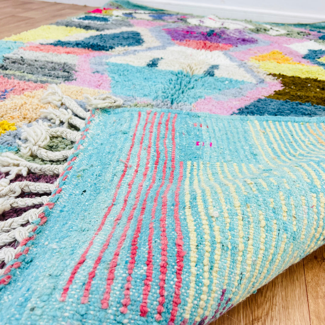 Colorful geometric vintage Moroccan wool rug with bold patterns and fringed edges, featuring turquoise, pink, and yellow hues.