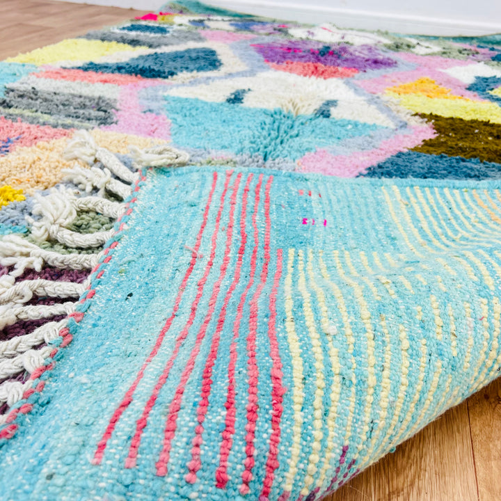 Colorful geometric vintage Moroccan wool rug with bold patterns and fringed edges, featuring turquoise, pink, and yellow hues.