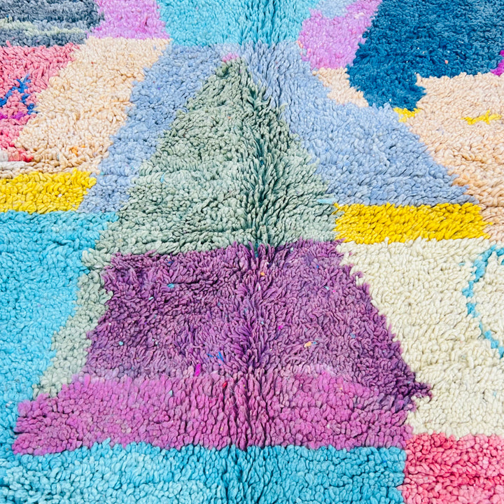 Colorful geometric Moroccan rug with turquoise, pink, yellow, and lavender artistic patterns.