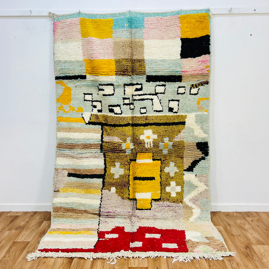 Vintage Moroccan rug featuring abstract tribal motifs in mustard yellow, red, pink, blue, and black. Handwoven Berber carpet.