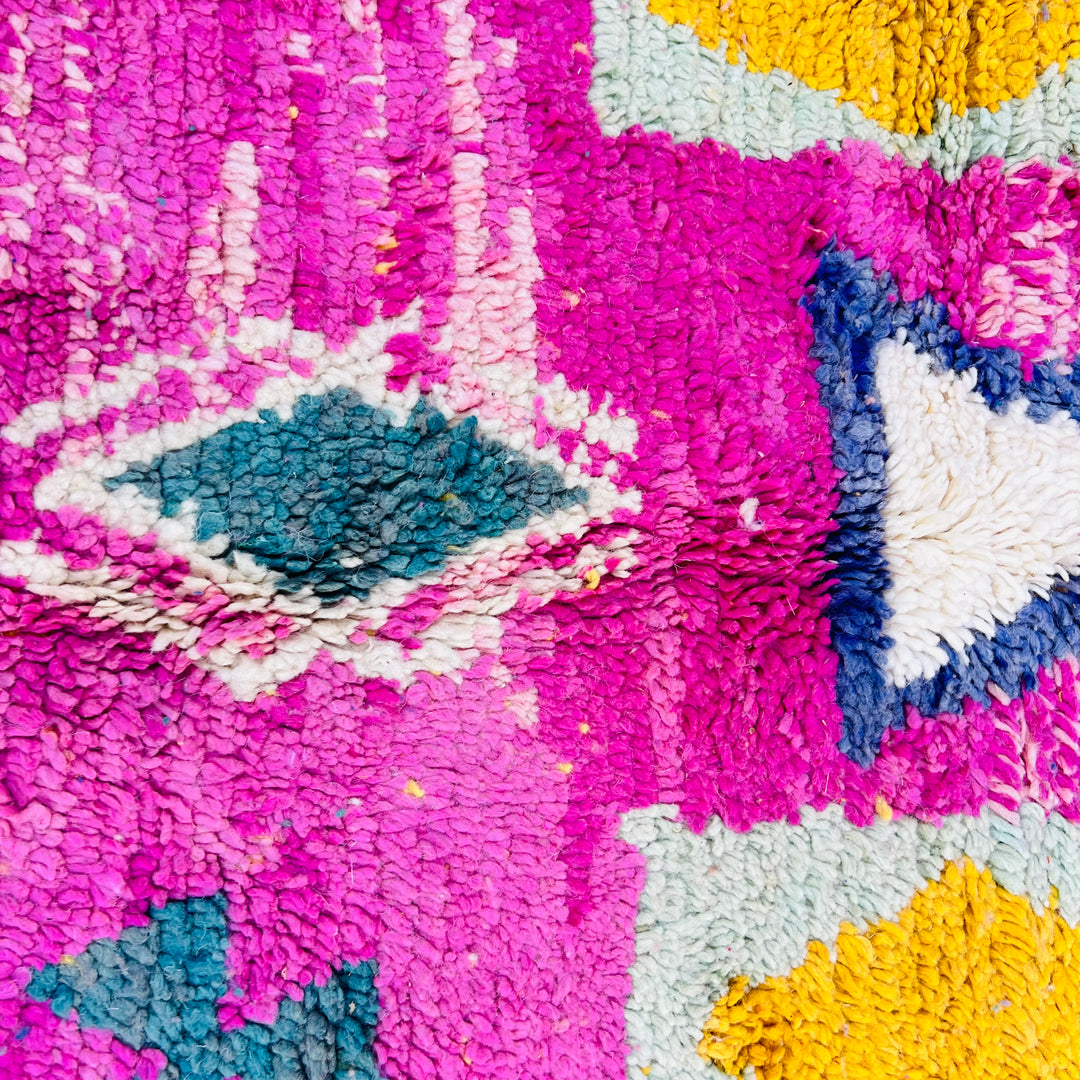 Close-up of a pink Moroccan rug with tribal symbols, featuring vibrant blue, mustard, and white motifs. Handwoven by Berber artisans.