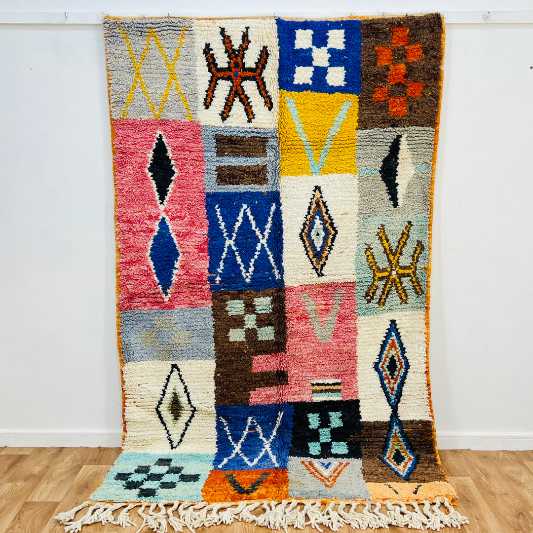 Colorful Moroccan patchwork wool rug with tribal symbols in vibrant red, blue, amber, and ivory. Handmade Berber artistry.