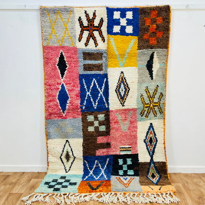 Colorful Moroccan patchwork wool rug with tribal symbols in vibrant red, blue, amber, and ivory. Handmade Berber artistry.