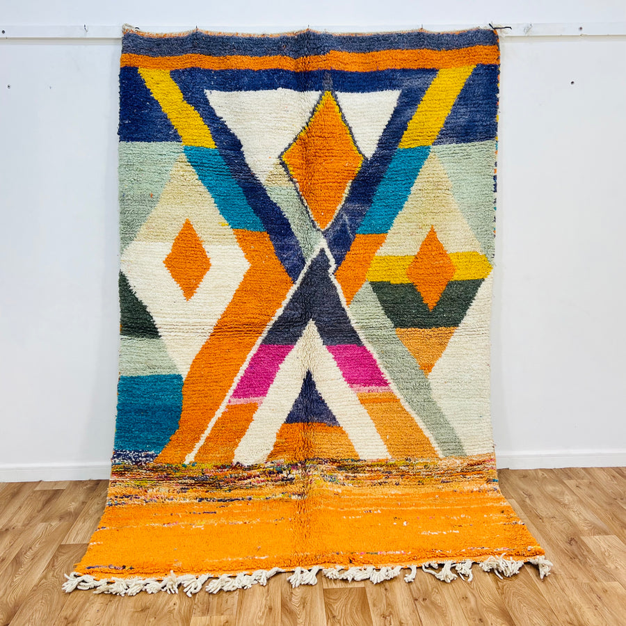 Colorful Moroccan wool rug with geometric diamond and X-shape motifs in orange, navy, fuchsia, ivory, and teal, 255x171 cm.
