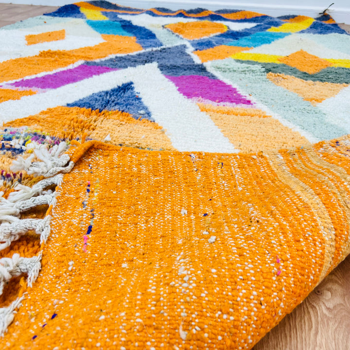 Large colorful Moroccan wool rug with bold geometric patterns in orange, navy, fuchsia, ivory, and teal.