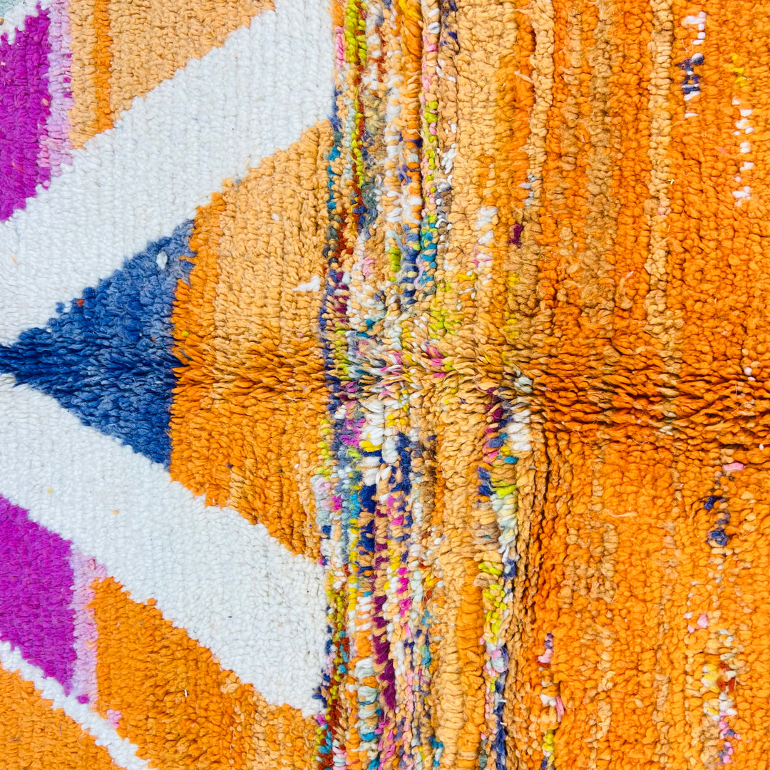Close-up of a colorful Moroccan wool rug featuring diamond motifs in orange, navy, fuchsia, ivory, and teal.