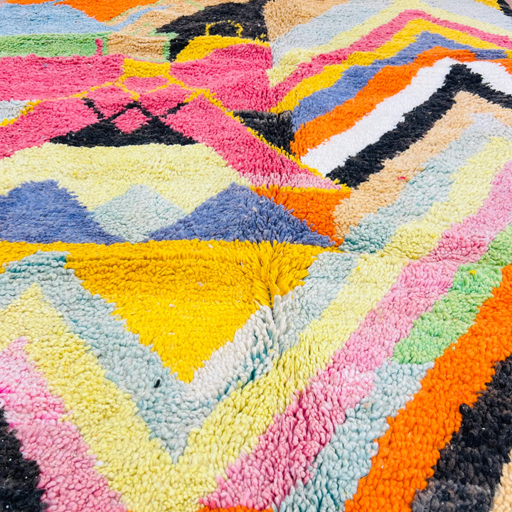 Colorful Chevron Moroccan rug with bold zigzag pattern, featuring pink, orange, yellow, black, and white handwoven by Berber artisans.
