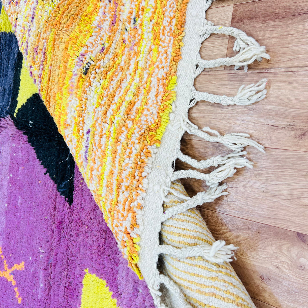 Close-up of a handmade vintage Moroccan rug with vibrant colors and tassels, embodying a sunset-inspired design and creative atmosphere.
